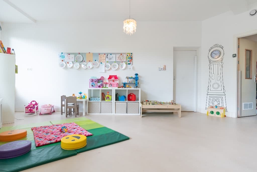 De groepsruimte met speelkleed, speelgoedkast en een klok op de muur