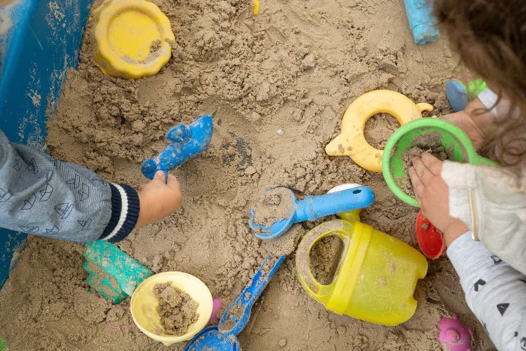 Kinderhanden met schepjes en emmertjes in de zandbak